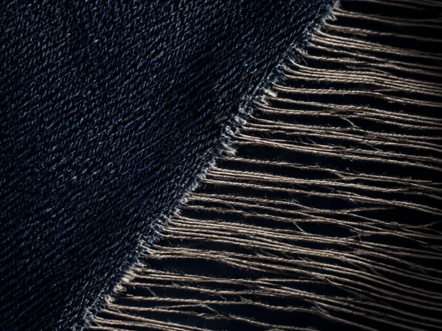 Dark indigo cloth meets loose pale threads along a diagonal edge against a black background.
